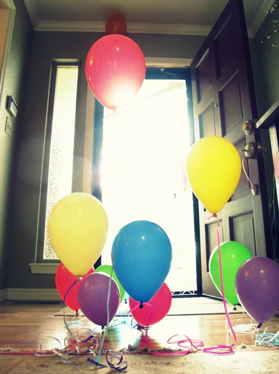 five balloons float near a doorway, with strings on the floor