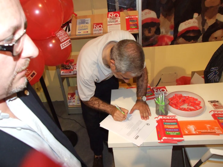 a man signing a receipt with red balloons on the background