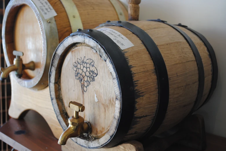 two wine casks on a wooden shelf next to some barrels