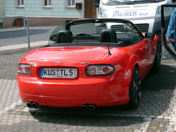 a red sports car is parked beside a white van