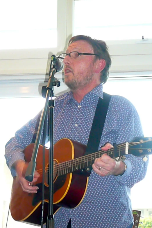 a man in glasses playing an acoustic guitar at a concert