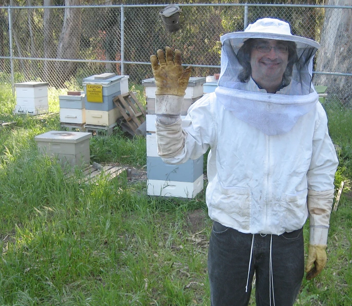 an elderly man in protective clothing holding up a beehive