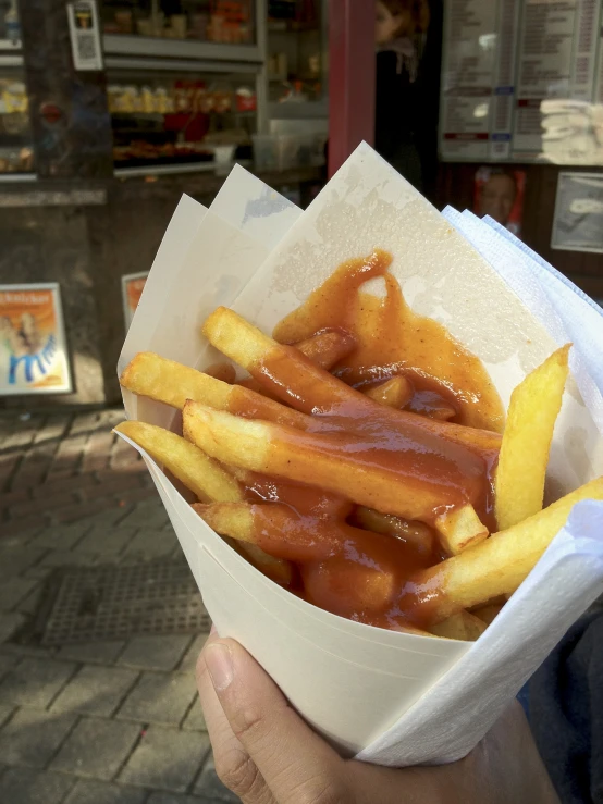 a hand holds up a tray full of french fries with sauce on them