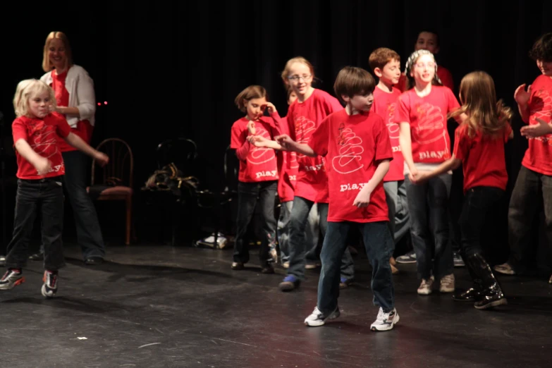 group of children wearing red shirts standing on stage