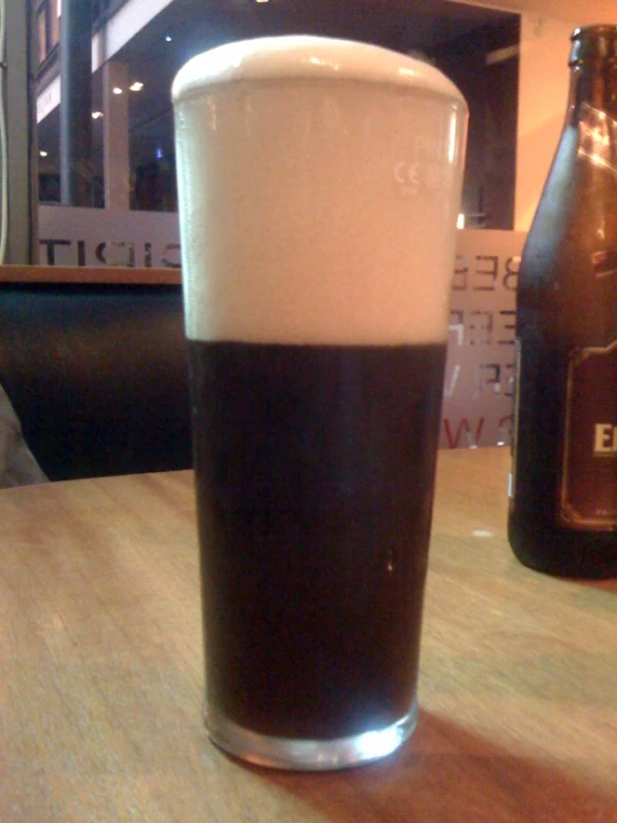 a dark colored drink sits on a table next to two empty beers