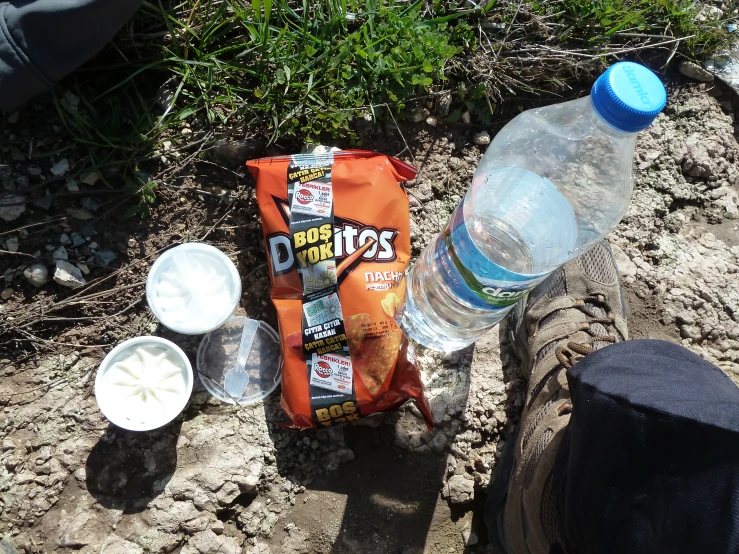 a person sitting on a dirt surface next to bottles and containers