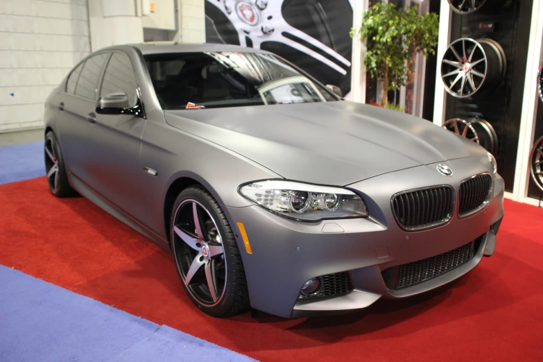 a grey car sitting on a red carpet in front of a wall with tires and planters