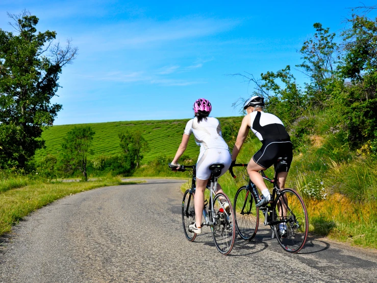 two people in wedding outfits on bikes riding down the road