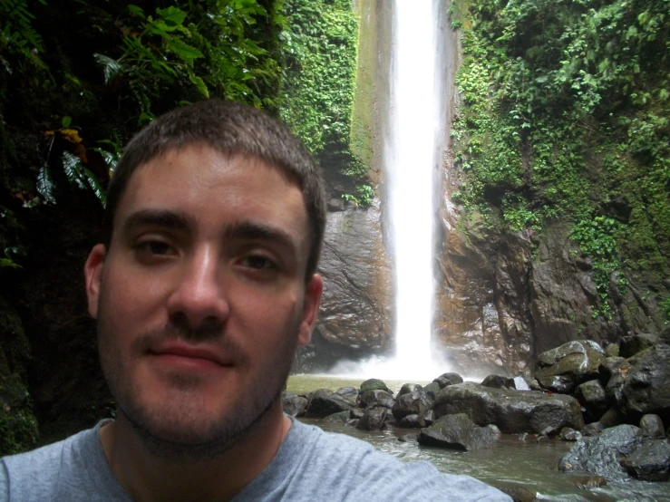 a man standing next to a waterfall with lots of greenery