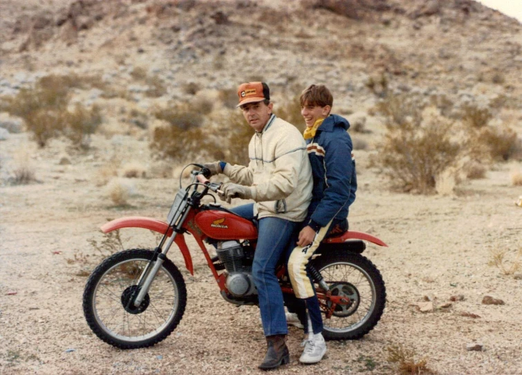 two people on a red motorcycle with desert in the background