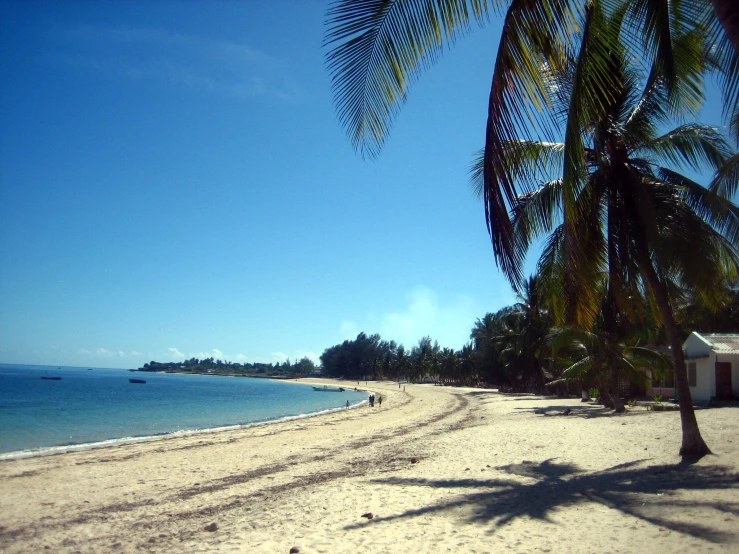 a sandy beach with a white house in the water and palm trees