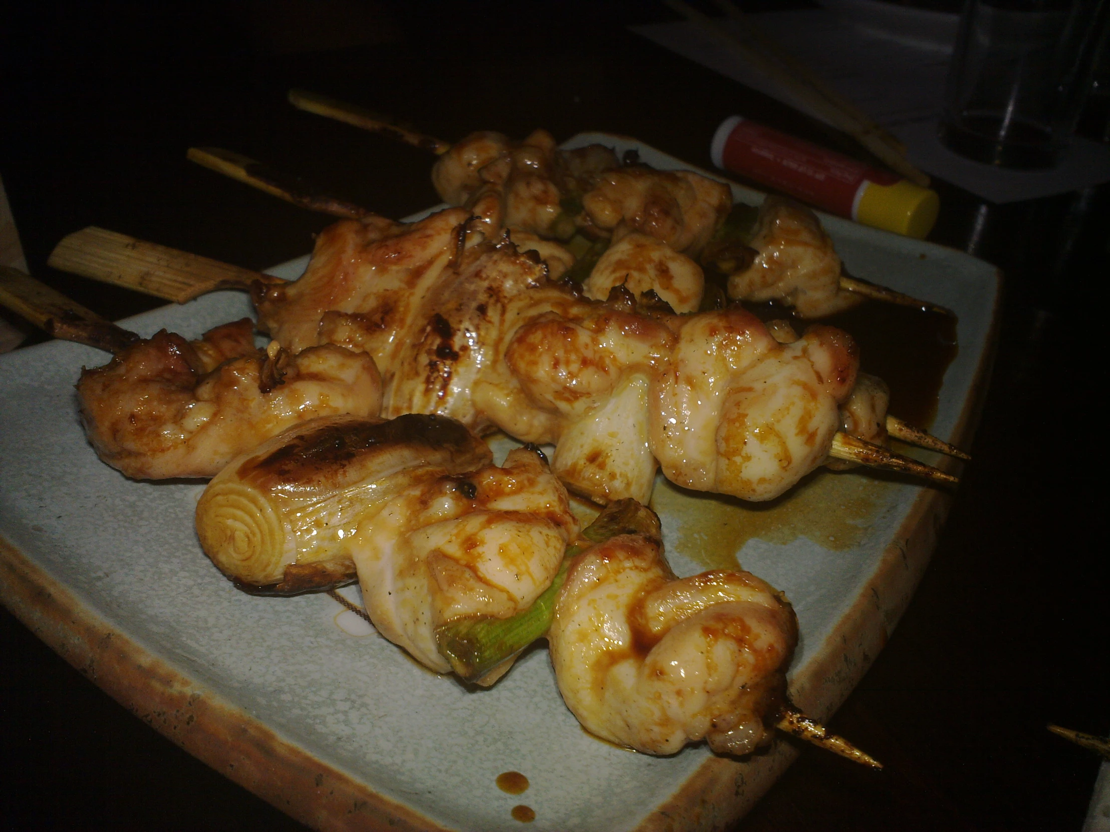 chicken skewers with sauce on a plate next to a bottle