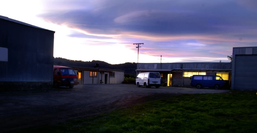 an empty field at night with two trucks parked on the ground and one truck parked in front of the building