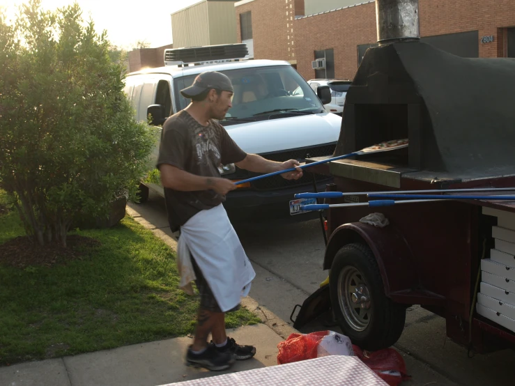 a man with a hat and apron stands next to an open car trunk