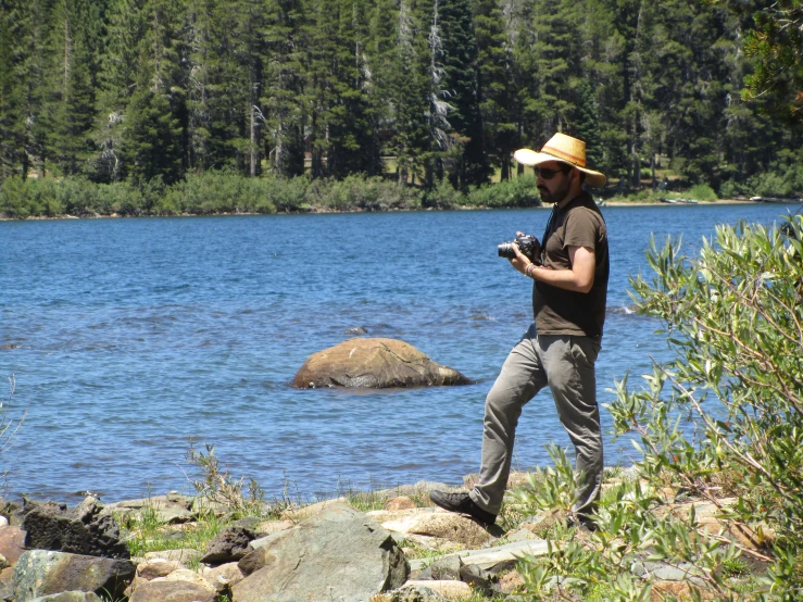 the man with a yellow hat and a camera is standing by the water