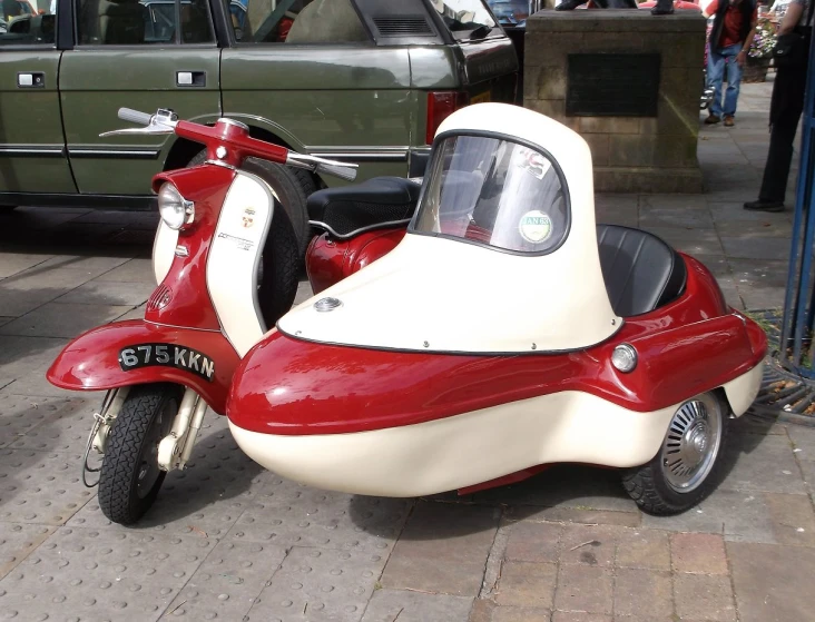 a red and white scooter parked next to a green pick - up truck