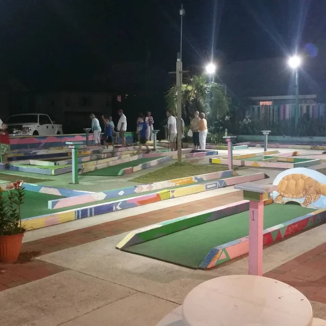 people gather on the artificial putting green at a mini golf course