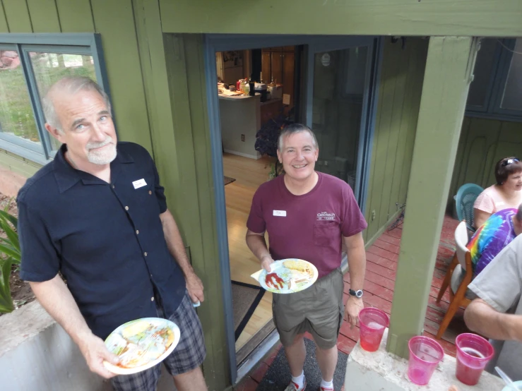 man and woman holding plates standing next to each other on porch