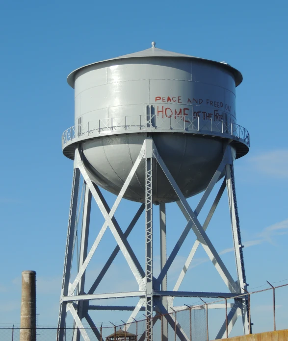 a gray water tower with writing on it in front of a blue sky