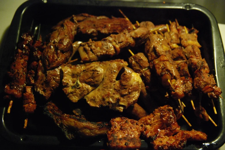 some meat sitting on top of skewers in a black pan