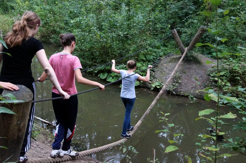 people walking across a suspension bridge in the woods