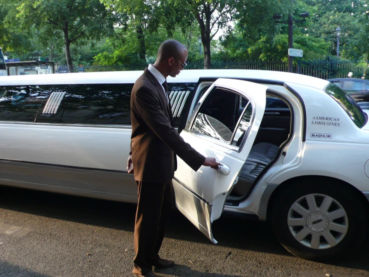 the man stands next to a white limousine in an open parking lot