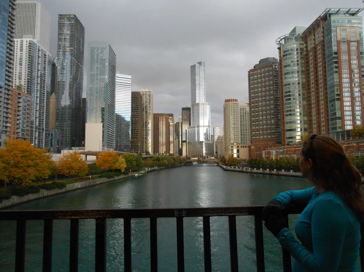 a woman stands near a river and city with a dark sky