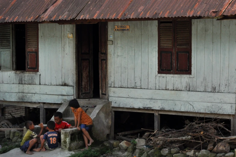 three young children sit on the side of two old wooden buildings