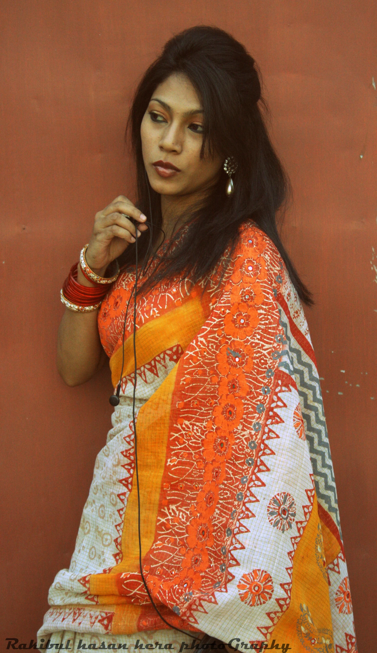 a woman with a large earbud sits by a wall