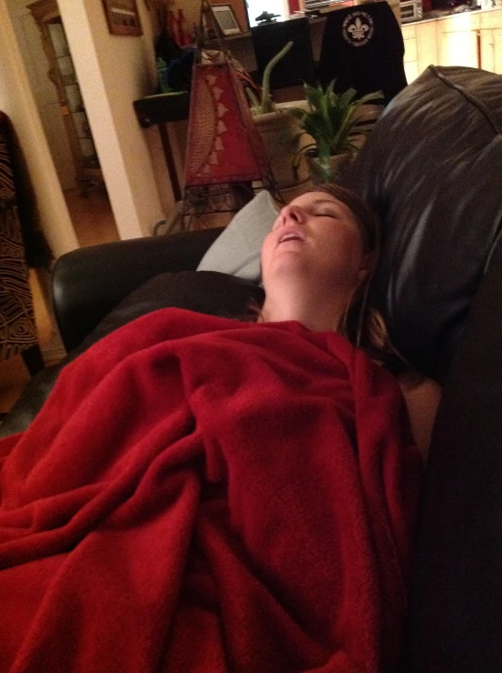 a woman laying on the couch in her living room covered in a blanket