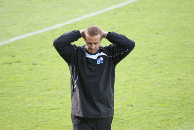 a man in black shirt looking at the ground holding his hair with both hands
