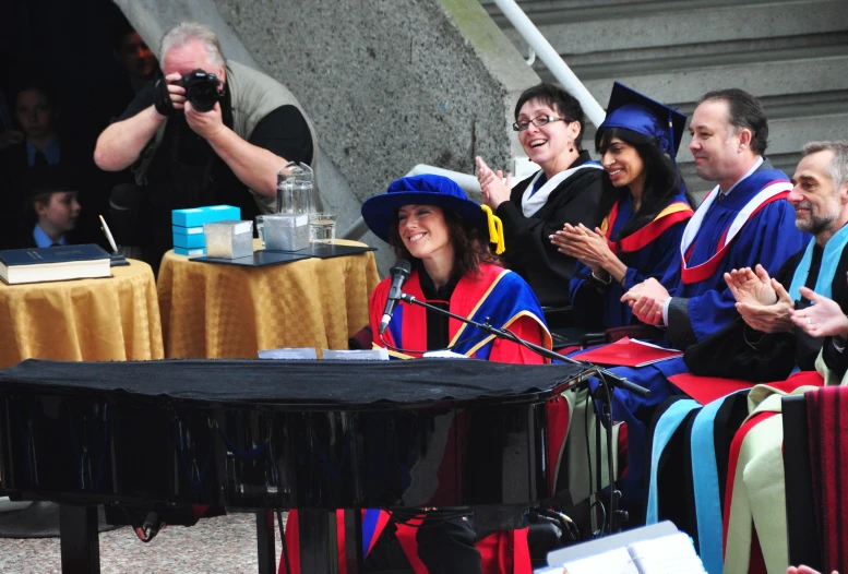 several people in graduation robes seated at a table with microphones