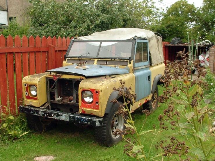 an old truck is parked on the grass near a fence