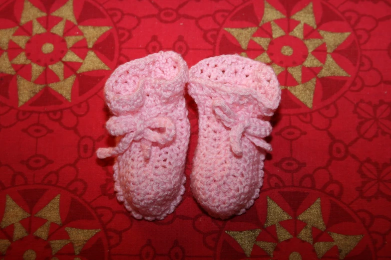 a crocheted pink pair of shoes on a red background