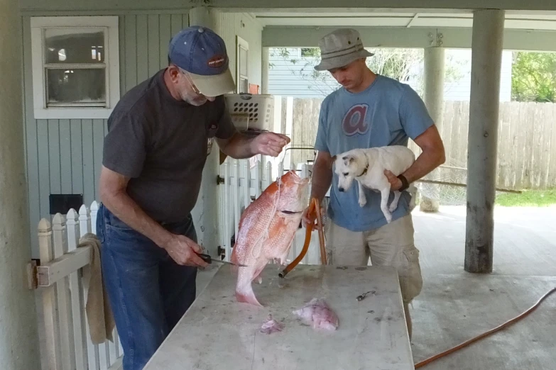 a man with a dog stands next to a fish while another holds up one