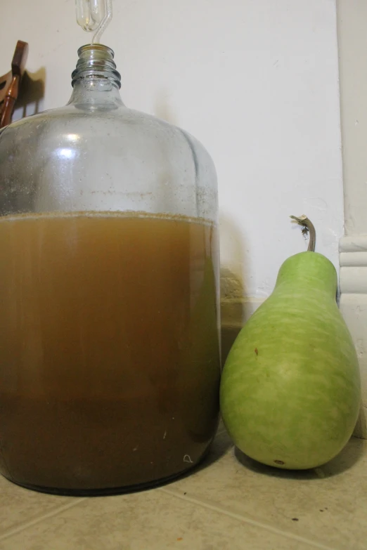 a glass bottle next to a green pear