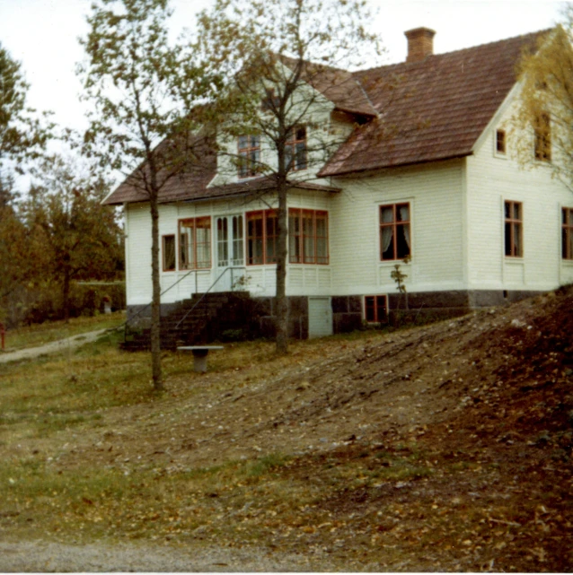 a white house sits in the grass and has red shutters