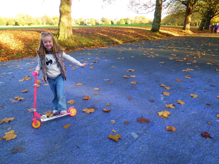 a girl rides her scooter through a leaf strewn park