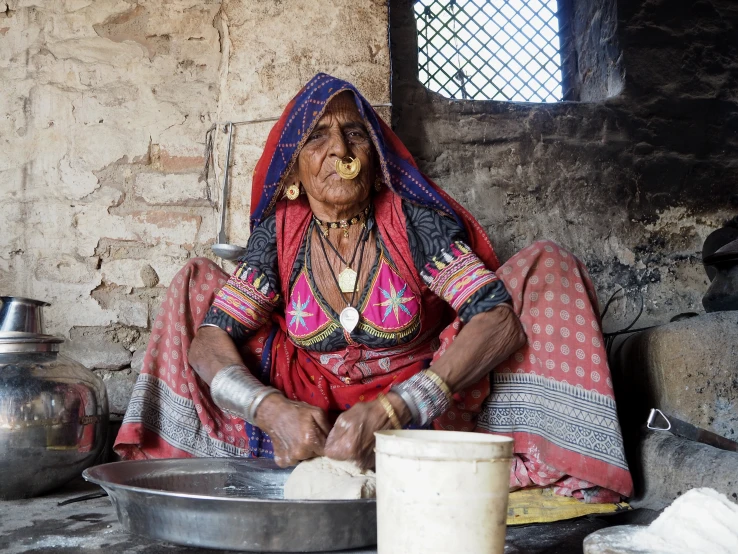 a woman with an orange necklace sitting in front of a silver dish and pots