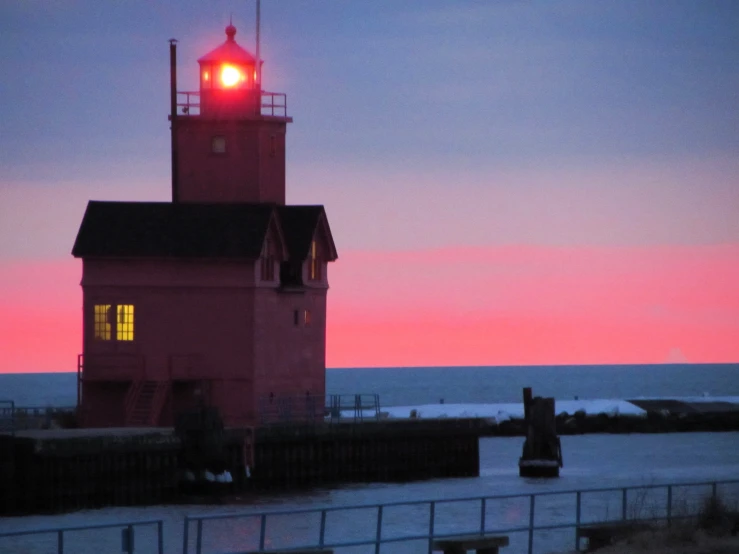 a red lighthouse sits near the ocean at sunset