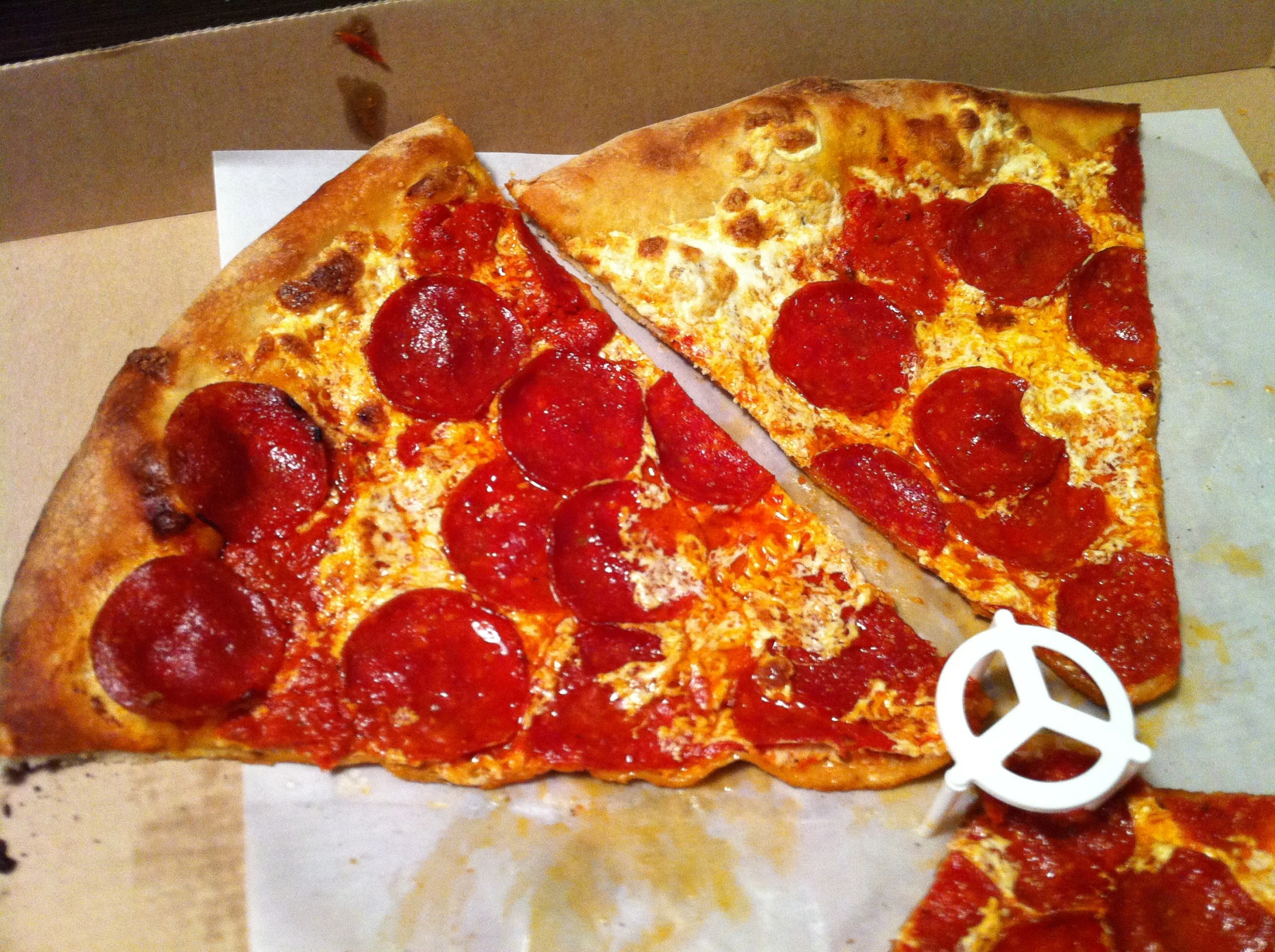 a slice of pepperoni pizza sits in front of the pizza cutter