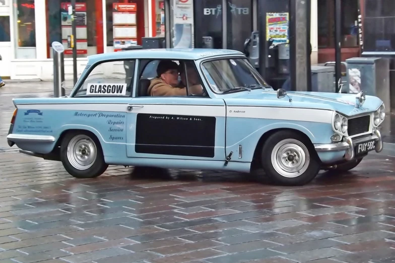 an old fashioned blue and white car is parked on a brick sidewalk