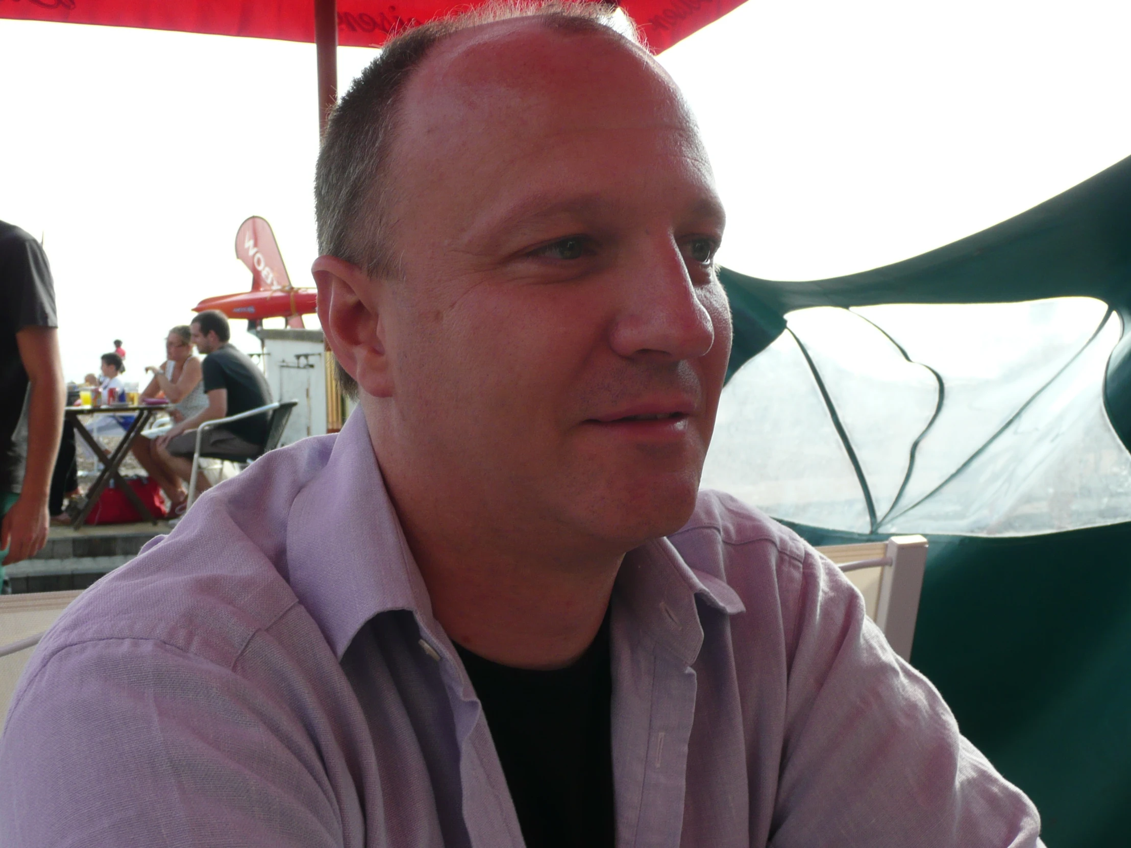 a man in a purple shirt sitting under an umbrella