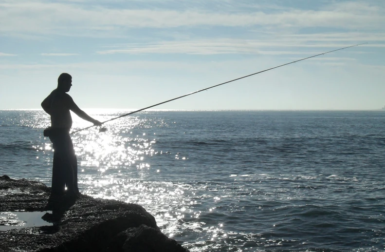 a man is fishing off of a cliff with the ocean in the background