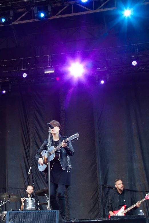 three people on stage playing guitar on a clear day