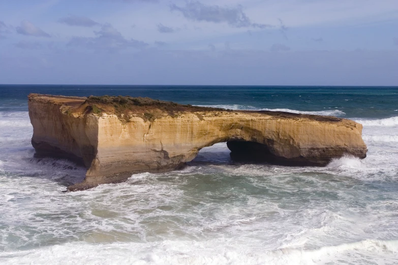 an arch shaped rock sits in the surf