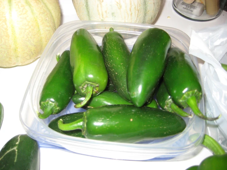 green peppers in a container are next to some squash