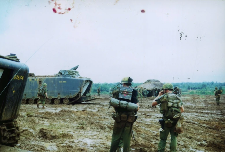 some military men standing in the mud near tanks