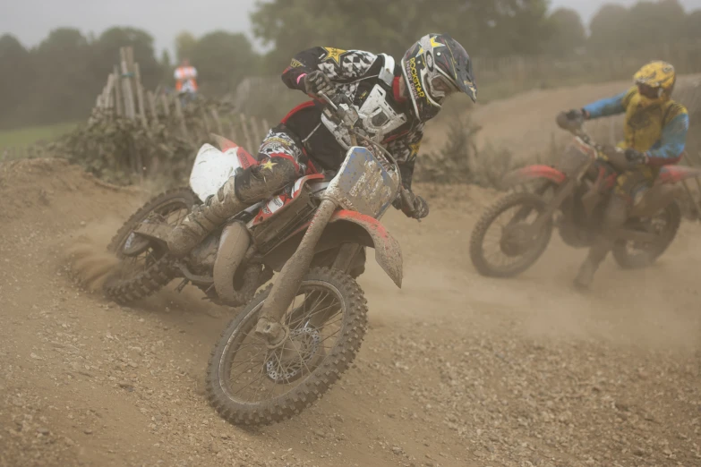 two dirt bikers with helmets on are kicking up dirt