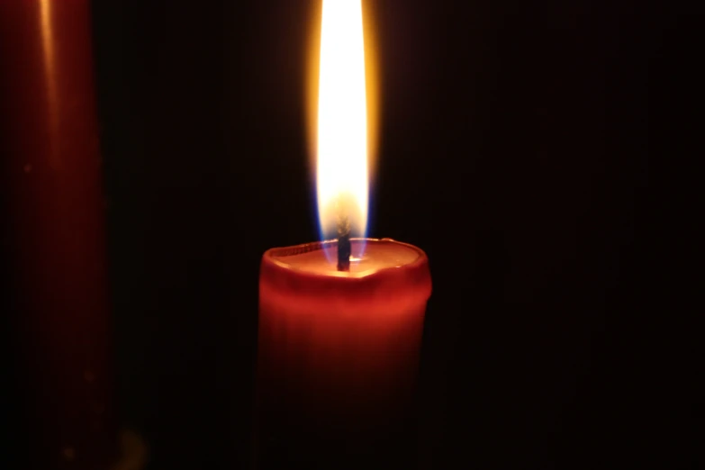 close up of a red candle with a bright lit candle